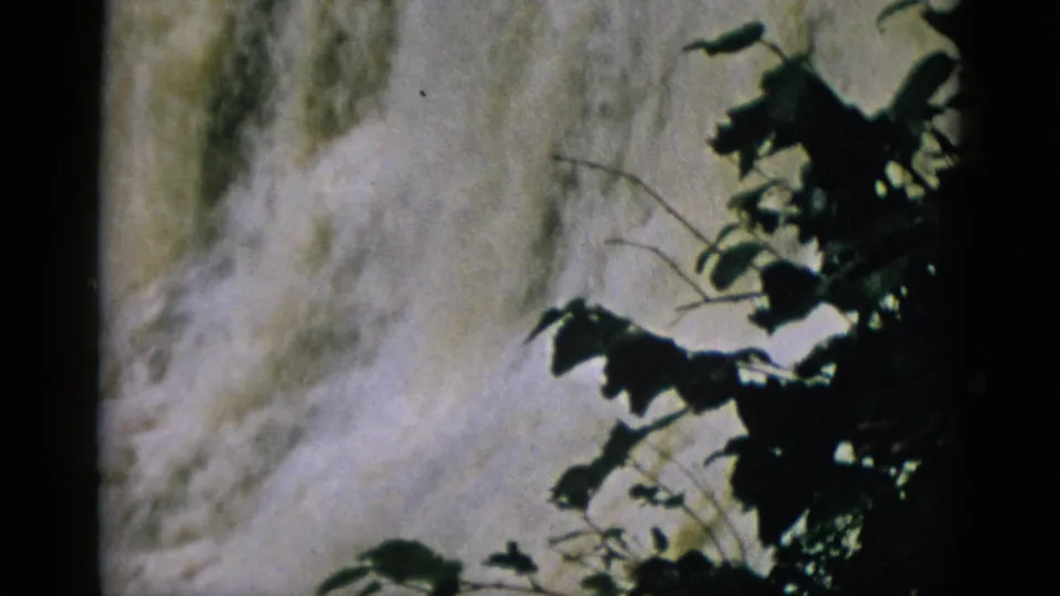 8mm film circa 1952, waterfall with bright mist patches and thin branch silhouettes in the lower foreground.