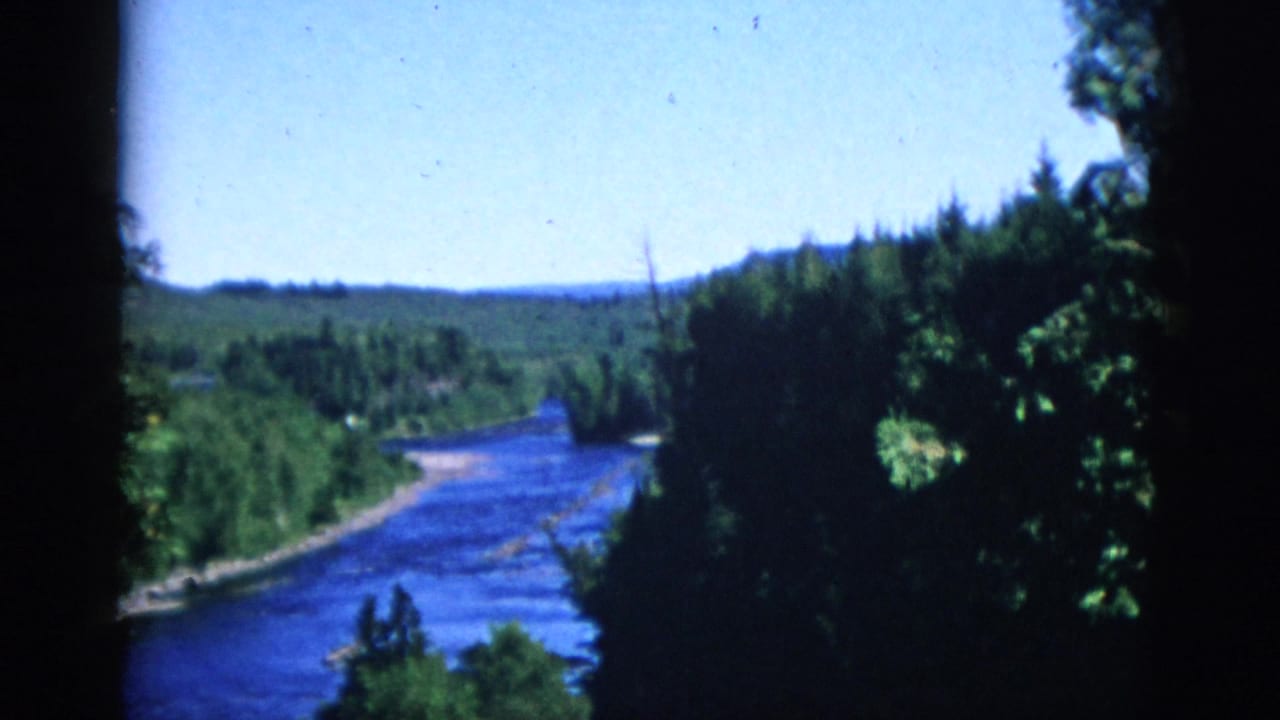 Elevated view of a wide blue river winding through boreal coniferous forest, Quebec, Canada, in 8mm home movie footage dated to circa 1952.
