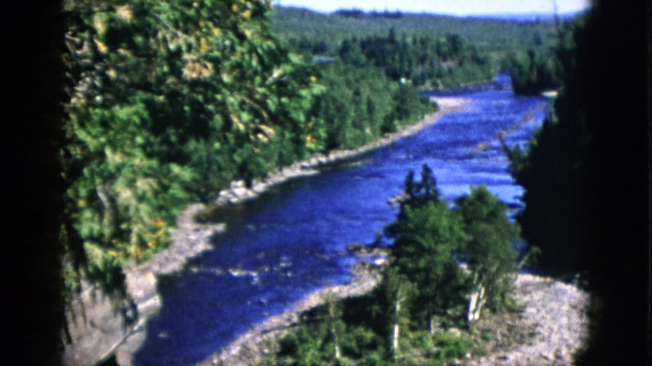 8mm color film, c.1952 Quebec — elevated pan opening frame showing a cobalt-blue river winding through coniferous forest with gravel shoreline.