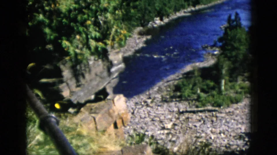 8mm film c.1952, Quebec — closing pan frame shows river receding into boreal valley with foreground timber and open sky above the treeline.