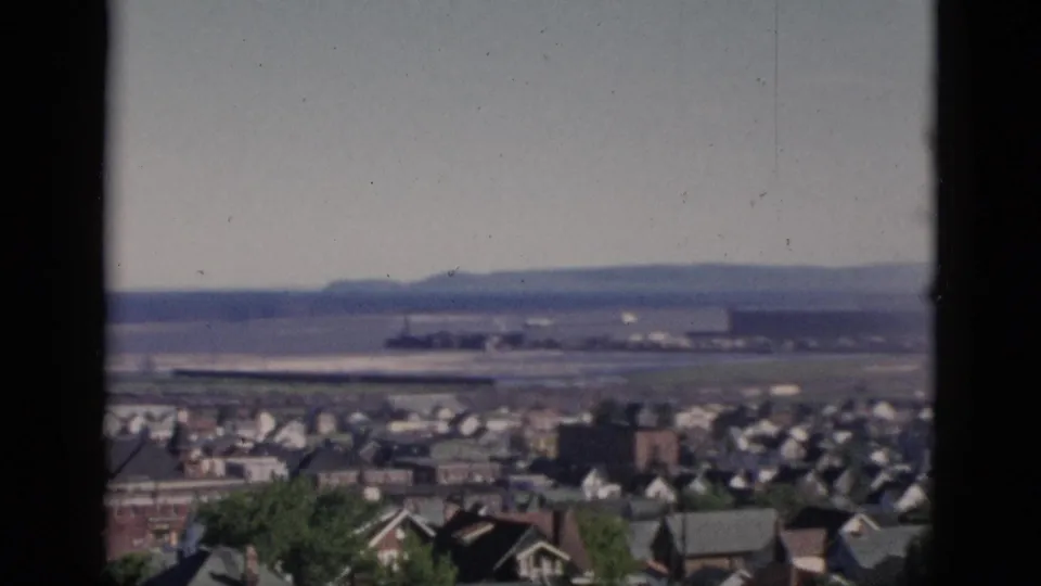 8mm color film, Quebec, Canada, 1952: camera has tilted upward, giving prominence to the open sky and wide flat distant expanse above the residential rooftops below.