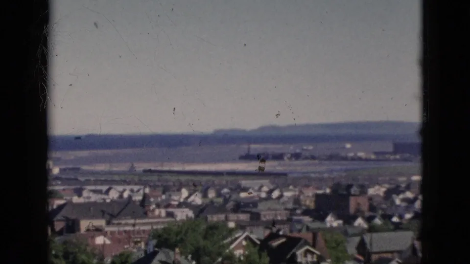 Final 8mm color film frame from Quebec, Canada, 1952 hilltop sequence: wide open sky above a residential grid and distant flat landscape stretching to low hills on the horizon.