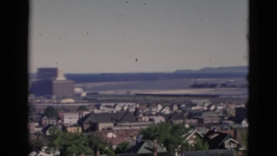 8mm pan at 0:02 reveals a large institutional or industrial building near the waterfront against low hills, with residential rooftops and tree canopy in the foreground, likely Quebec circa 1952.