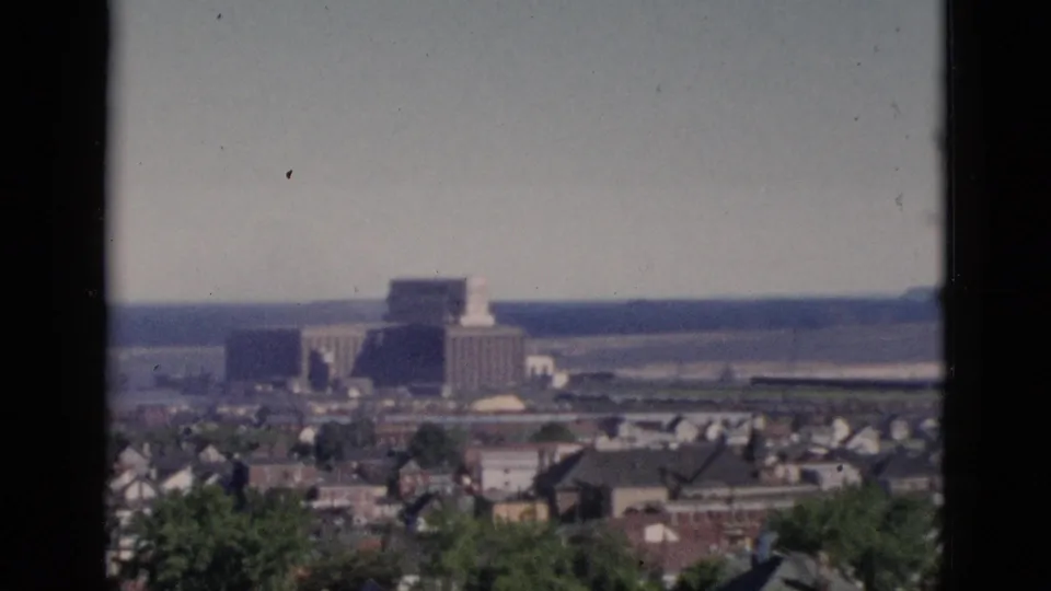 Final 8mm pan frame over Quebec circa 1952, showing residential rooftops, a large institutional building near the waterfront, and low hills receding into hazy distance.