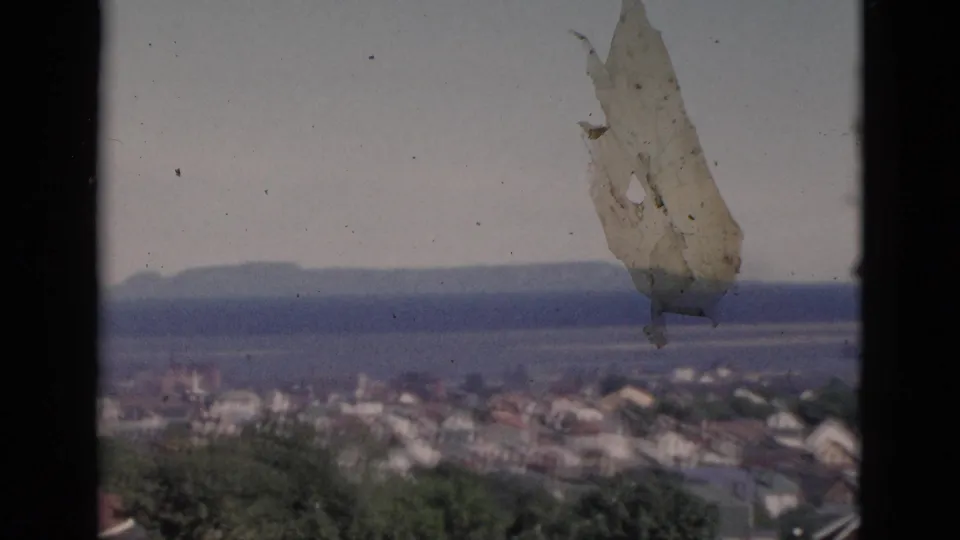 Quebec townscape circa 1952 with a prominent white irregular form — possibly a sail, fabric, or film-plane artifact — briefly visible through the window above the roofline