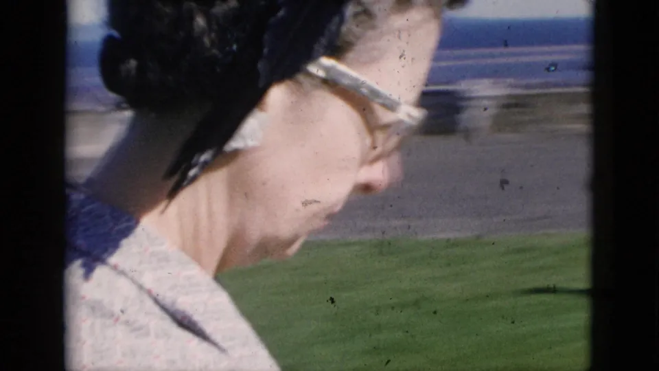Candid close-up profile of a middle-aged woman in cat-eye glasses, with visible 8mm film grain and dust marks; Quebec, Canada, circa 1952.