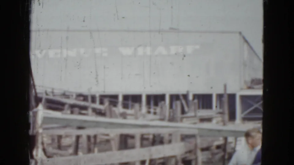 8mm home movie frame, c. 1952, New Orleans — Venice Wharf building and dock, with a figure in light-colored period clothing partially visible at the right edge.