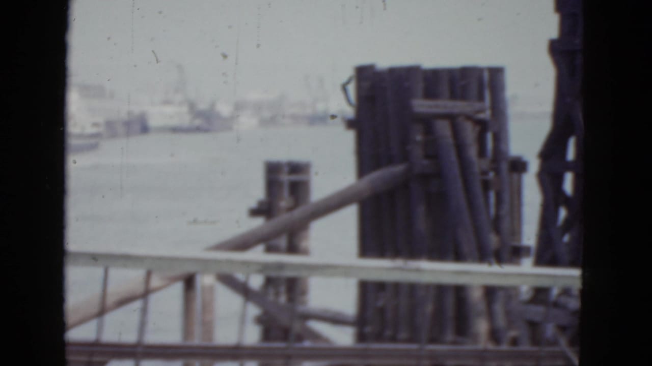 Wooden pier pilings and railing seen through dark vertical framing at a harbor.
