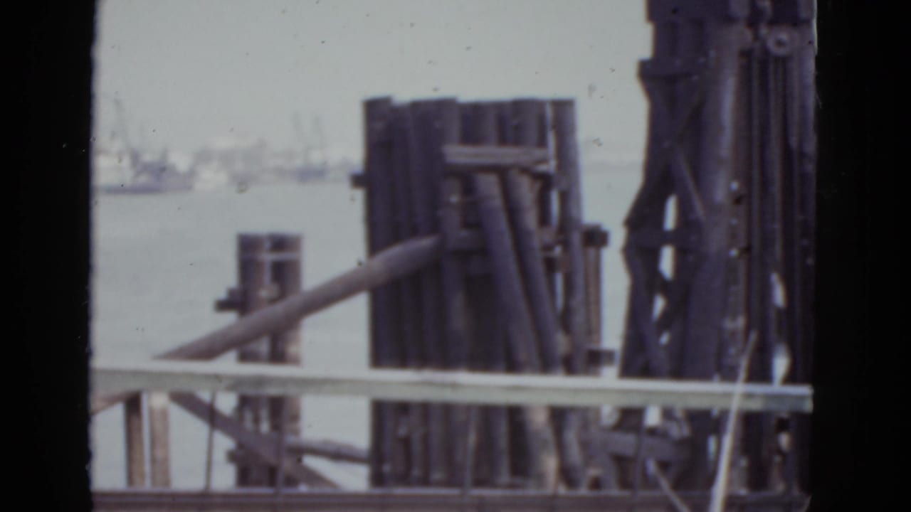 Harbor pier structure with timber bracing, railing, water, and distant vessels.