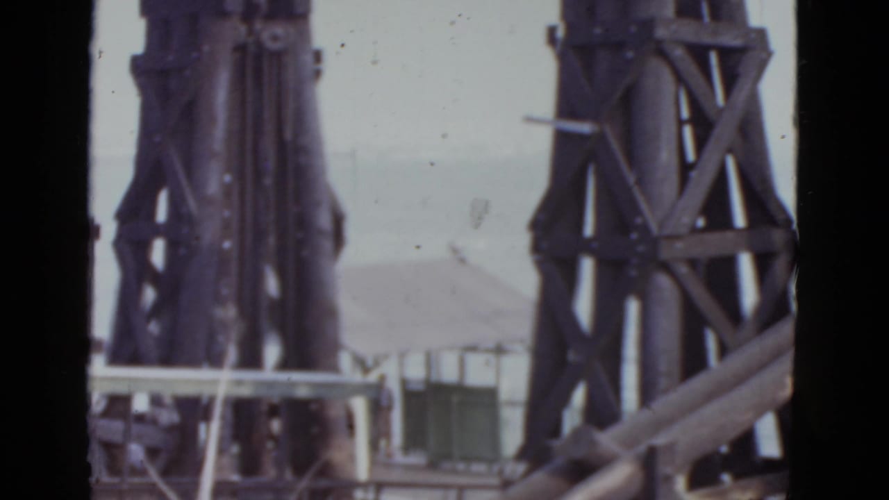 Steel lattice towers frame a sloped-roof building, with pale railing and structural members in the foreground.