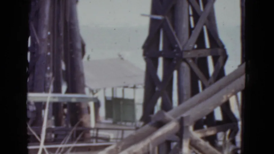 1952 New Orleans 8mm frame showing close steel bridge framework, angled members, a pale platform edge, and a low building behind.