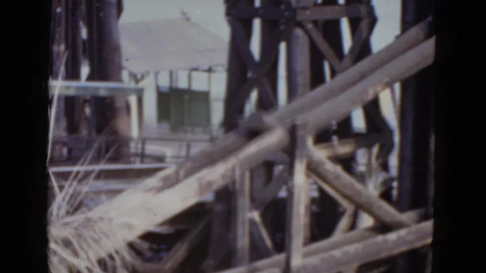 1952 New Orleans 8mm frame with diagonal bridge members crossing the foreground and dark steel latticework beside a background structure.