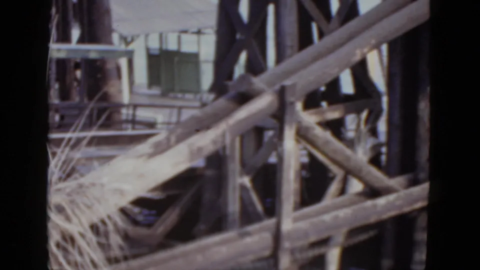 Close-up of weathered wooden dock cross-bracing and dark pilings at water level, New Orleans area, from a 1952 8mm home movie.
