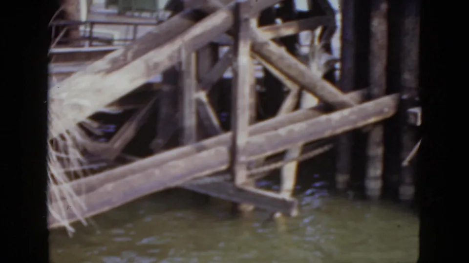 Weathered wooden pier substructure over murky water shot close from water level, from a 1952 New Orleans waterfront 8mm home movie.