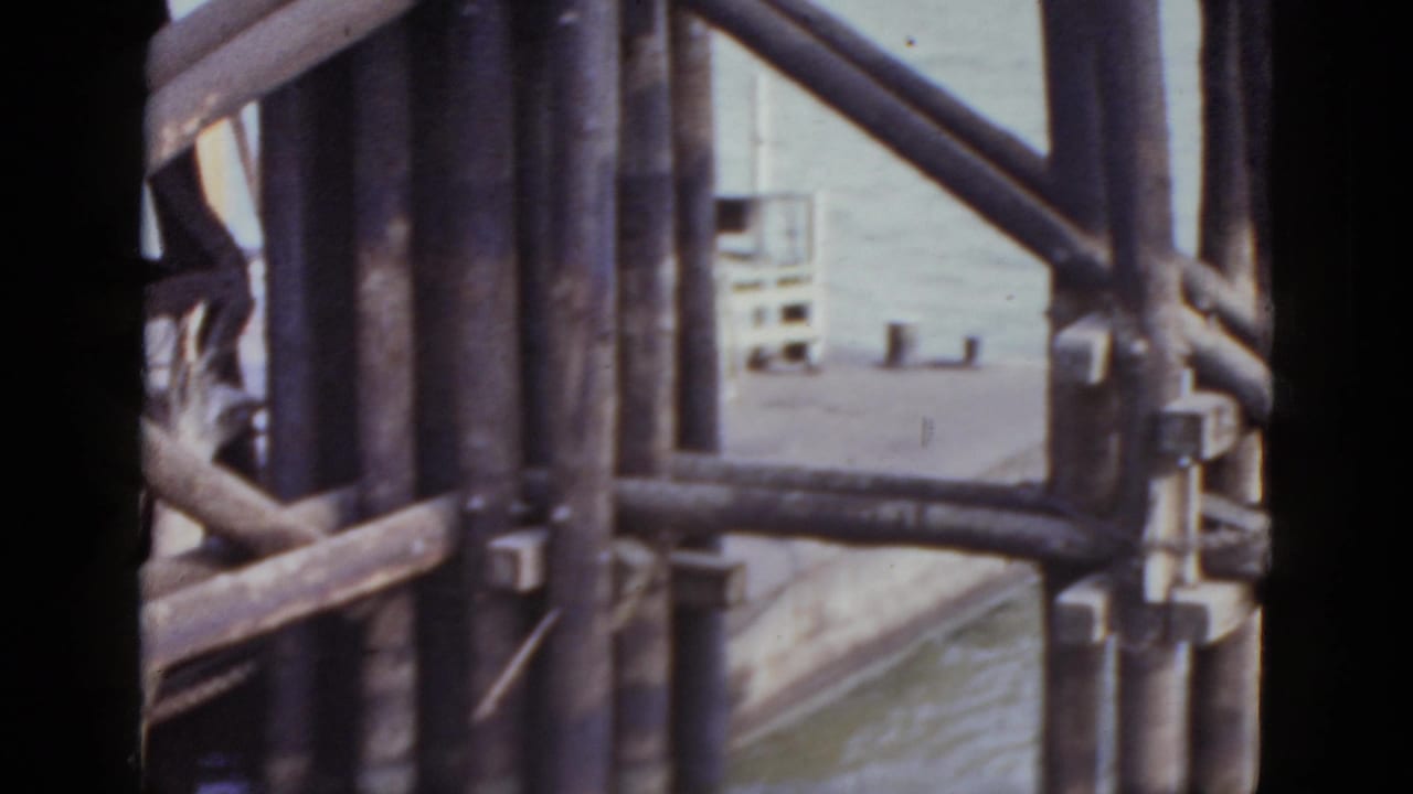 Large dark wooden structural beams fill the foreground; water and a partially visible building appear in the background.
