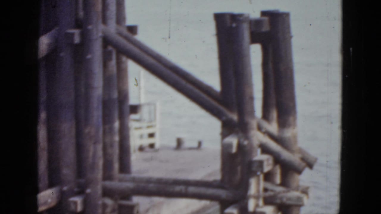 Dark wooden structural beams dominate the foreground with a building and water partially visible behind them.