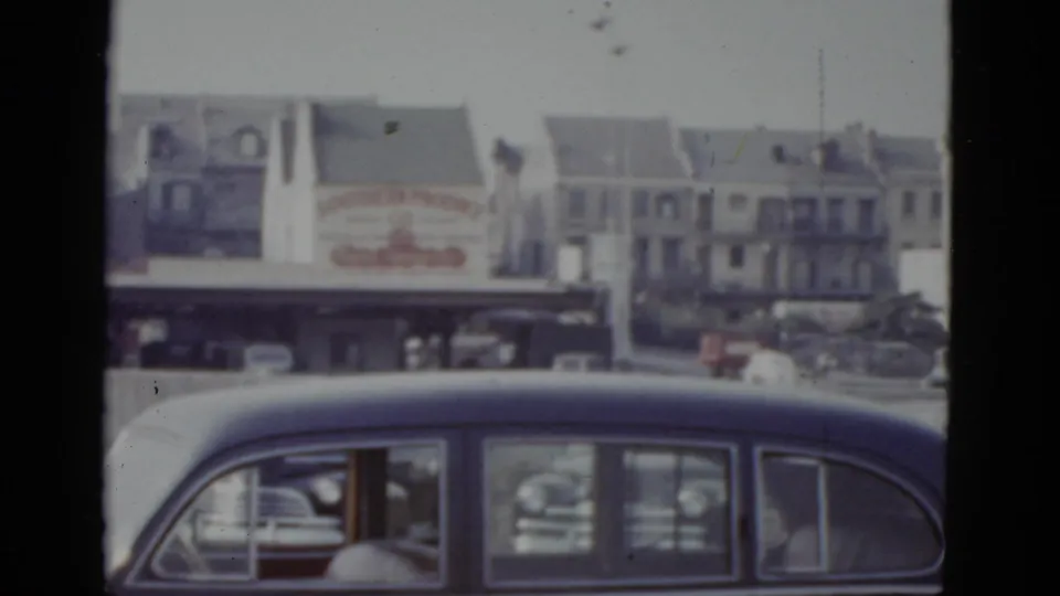 Final 8mm frame circa 1952 New Orleans: billboard and residential buildings, standing figure in white in mid-ground, dark blue sedan in lower frame.