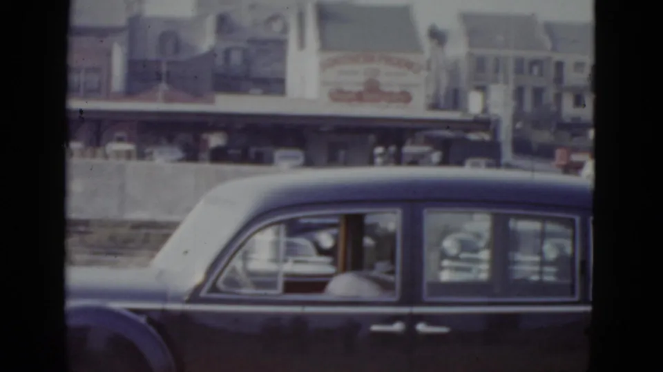 Dark American sedan in congested traffic with multi-story brick buildings and a white steeple visible in background; New Orleans, circa 1952 per clip metadata.