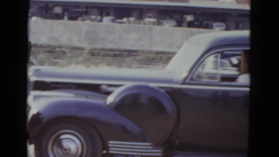 Rear quarter of an early-1950s American sedan with chrome multi-spoke hubcap and rounded fender; concrete barrier and commercial buildings visible behind; New Orleans, 1952 per metadata.