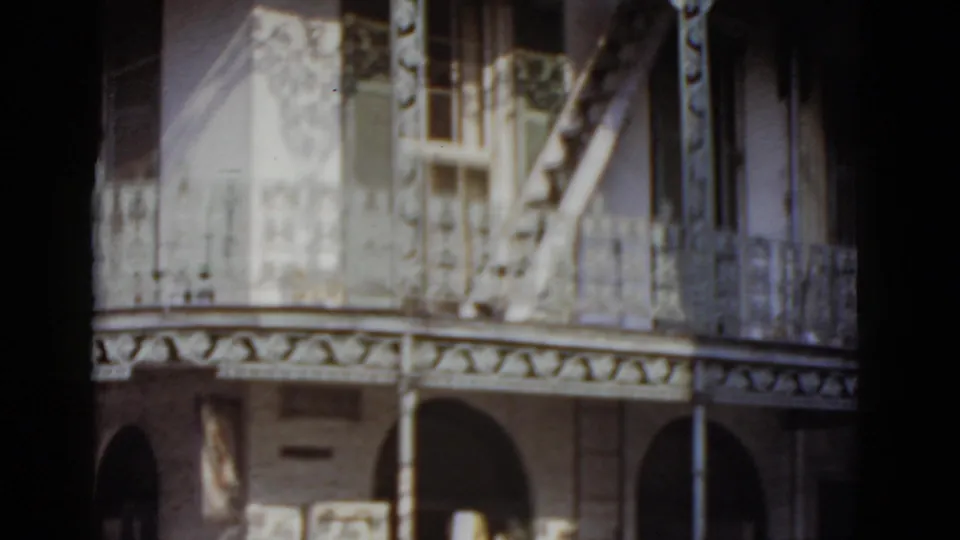 Decorative wrought-iron upper balcony and arched arcade of a New Orleans French Quarter-style building, shot on 8mm color film circa 1952.