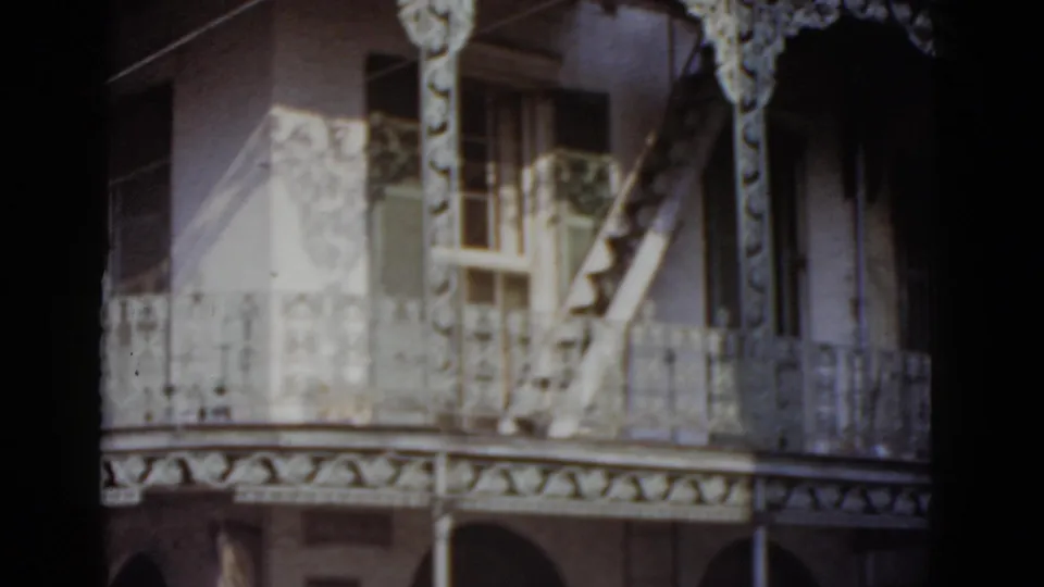Upper facade of a New Orleans ornate residence, circa 1952, showing cast-iron balcony railings, a rosette-pattern frieze, arched openings, and a wooden external staircase.