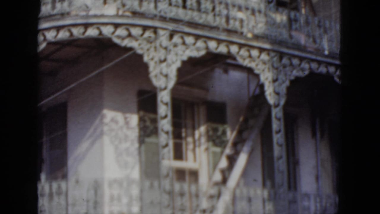 Continued pan of an ornate multi-story facade showing cast-iron balconies, decorative frieze, and arched openings on 8mm film.