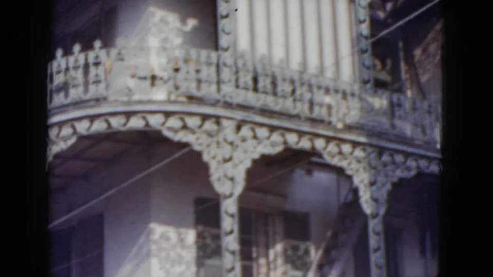 Lower balcony tier of the New Orleans ornate residence, circa 1952, with prominent curved cast-iron railing, decorative frieze, and shuttered openings in dappled sunlight.