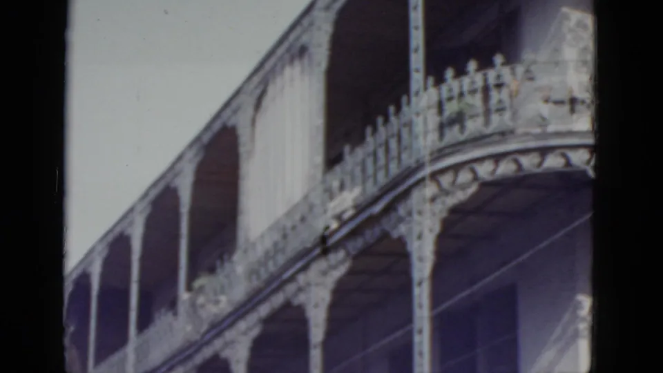 8mm home movie frame circa 1952 showing lower two stories of an ornate cast-iron gallery building in New Orleans, with curved arch supports and spindle railings.
