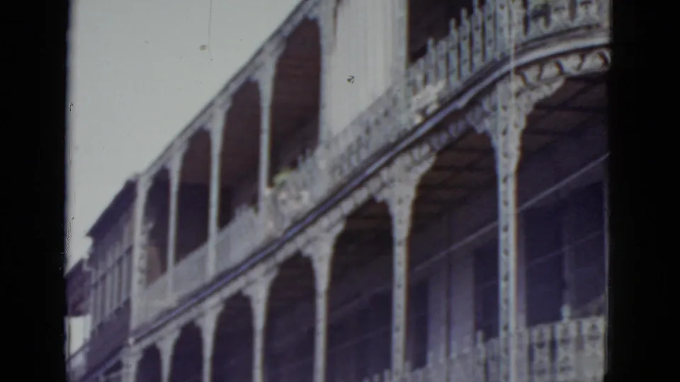 8mm home movie frame circa 1952 showing a broad view of a two-story cast-iron gallery with multiple arched openings on a New Orleans downtown facade.