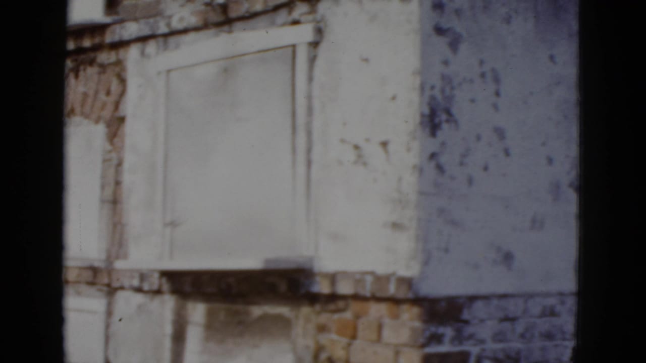 Close view of peeling white plaster and exposed brick on a building facade with ornamental arched window surrounds.