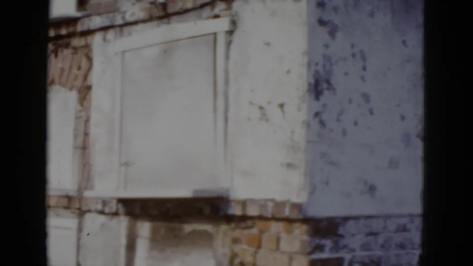 Deteriorating white-painted brick facade with arched ornamental moldings around sealed windows, New Orleans circa 1952, 8mm film.