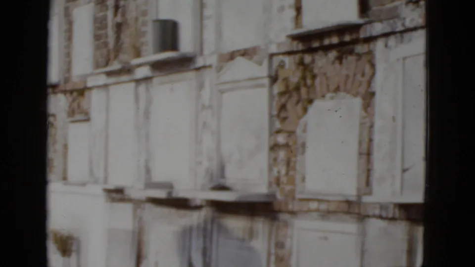 Deteriorating New Orleans building facade with sealed arched windows and a possible window-mounted AC unit, circa 1952, 8mm color film.