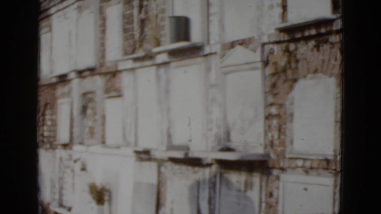 Rows of white plastered above-ground vault-like structures with arched rectangular niches, possibly a New Orleans cemetery wall, 8mm color film.