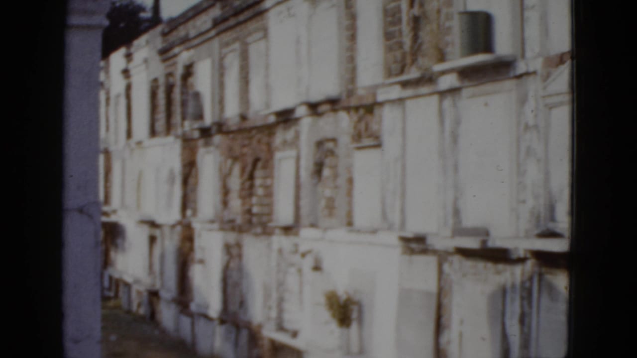 Continued view of white plastered above-ground vault structures with arched niches, slight camera repositioning visible, 8mm color film.