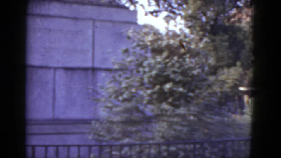 Stone pedestal base amid mature garden trees, likely the base of the equestrian monument visible later, in a New Orleans public garden, 1952 8mm footage.