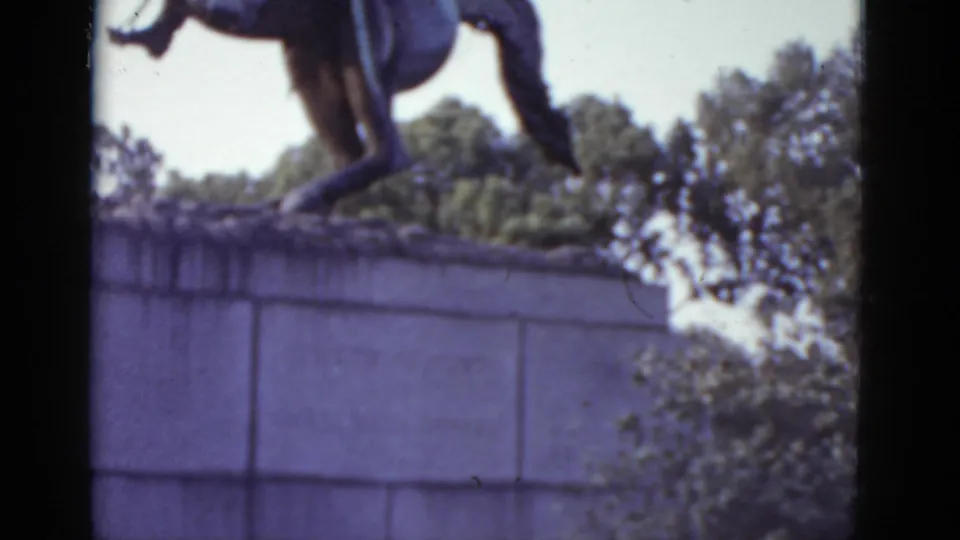 Horse hooves and lower rider of a large equestrian statue on a stone pedestal, bright sky behind tree canopy, appearing to be in a New Orleans public garden, 1952.