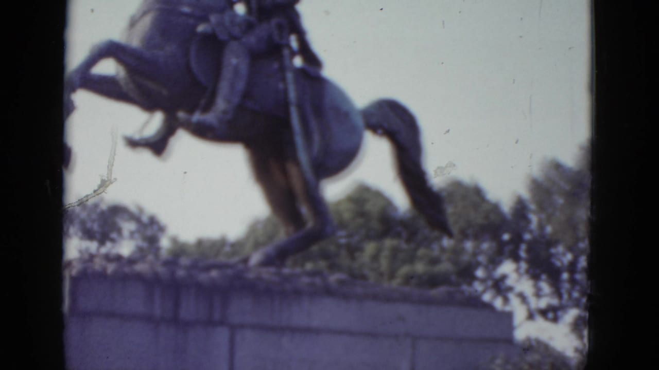 Bronze equestrian statue of a uniformed rider on a rearing horse, shot close-up from below on 8mm film with a heavy purple color cast.