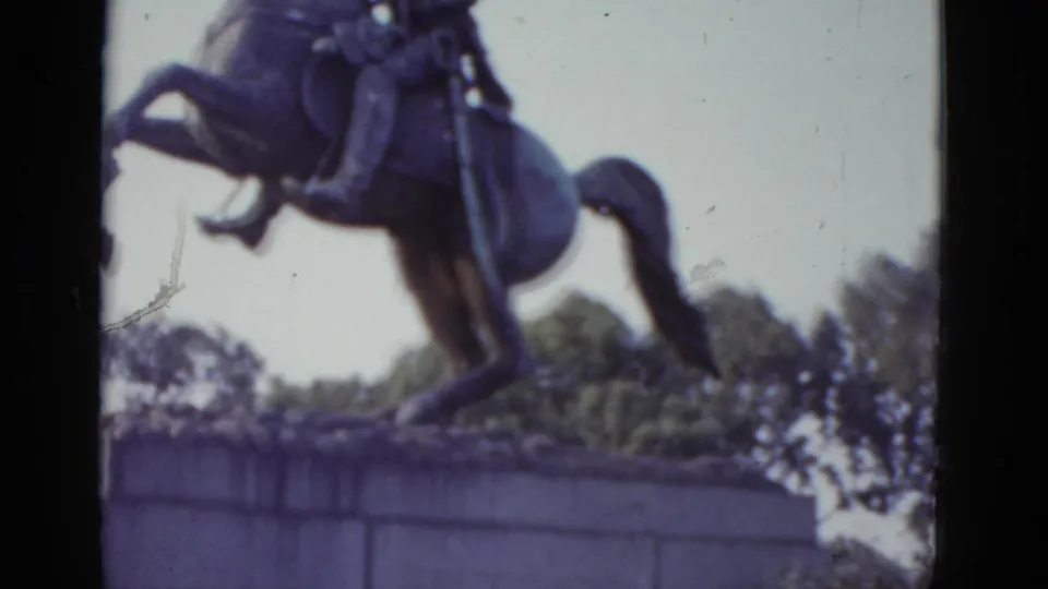 Close-up 8mm view of an equestrian statue, likely in New Orleans' Jackson Square circa 1952, showing a uniformed rider on a rearing horse against a pale overcast sky.