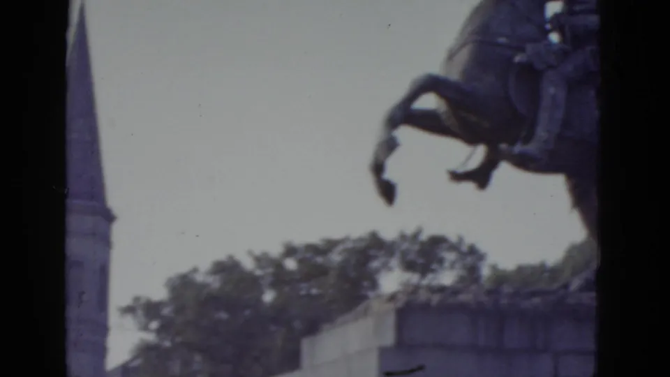 8mm home-movie frame of an equestrian statue in New Orleans, circa 1952, with a partial steeple or spire entering from the left edge of frame.