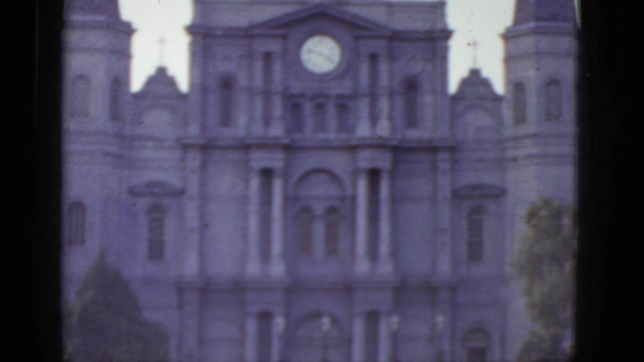 8mm home movie frame circa 1952 showing the full Gothic cathedral facade in New Orleans, circular clock centered above the main entrance, tree visible at right.