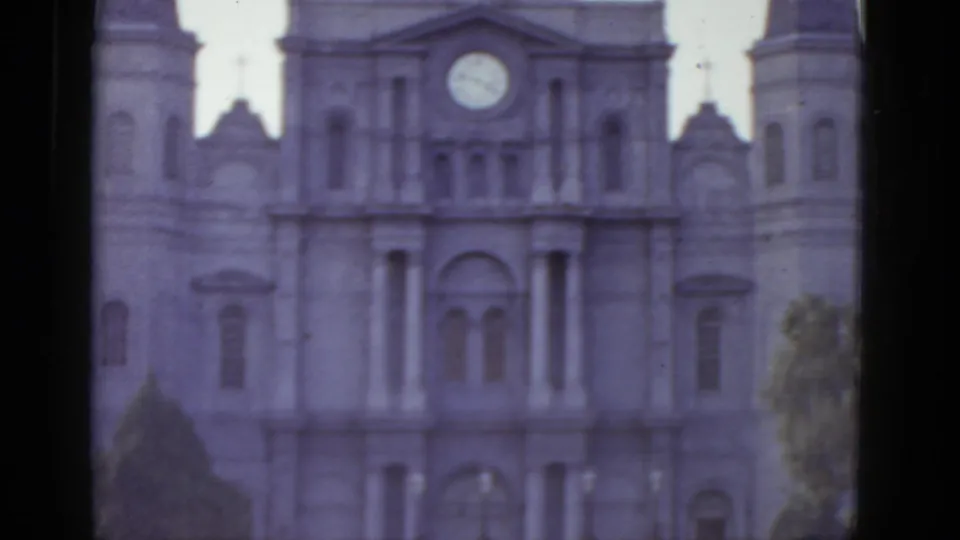 8mm home movie frame circa 1952 showing the full Gothic cathedral facade in New Orleans, circular clock centered above the main entrance, tree visible at right.
