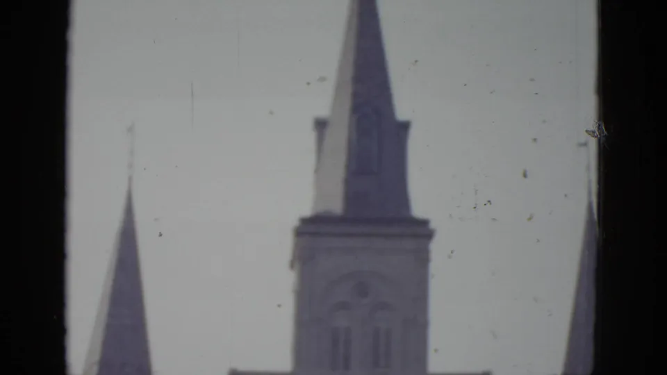 Final 8mm tilt frame circa 1952, New Orleans cathedral — spire tips isolated against overcast sky, film grain and scattered dust specks visible.
