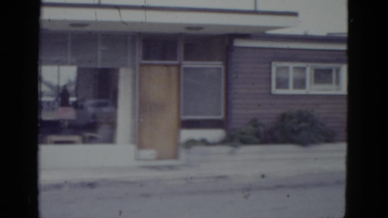 Mid-pan view of the same commercial building facade showing a plate-glass window, wooden door, and a vehicle reflected in the glass.