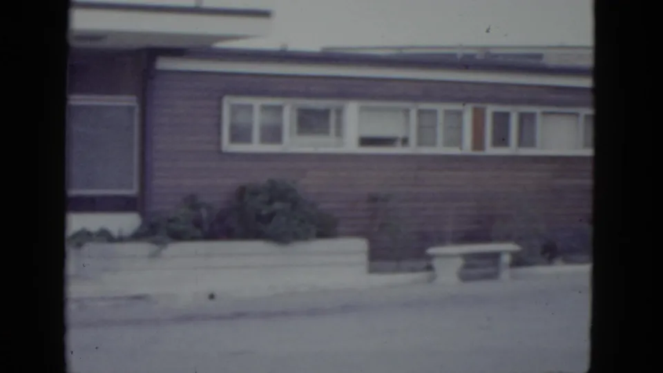 Final 8mm frame of 1952 New Orleans commercial building pan; louvered windows, low concrete planter with shrubbery, and a small bench at the planter edge.