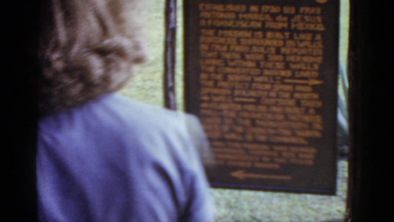 Adult visitor seen from behind pausing before the San José Mission interpretive sign; 8mm color home movie, circa 1952.