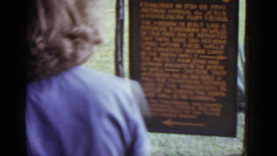 Adult visitor seen from behind pausing before the San José Mission interpretive sign; 8mm color home movie, circa 1952.