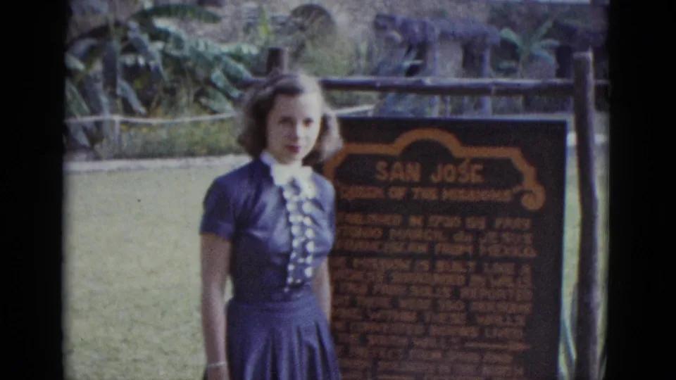 Young woman in early-1950s blue pleated skirt and ruffled blouse posed before the San José Mission 'Queen of the Missions' marker, circa 1952.