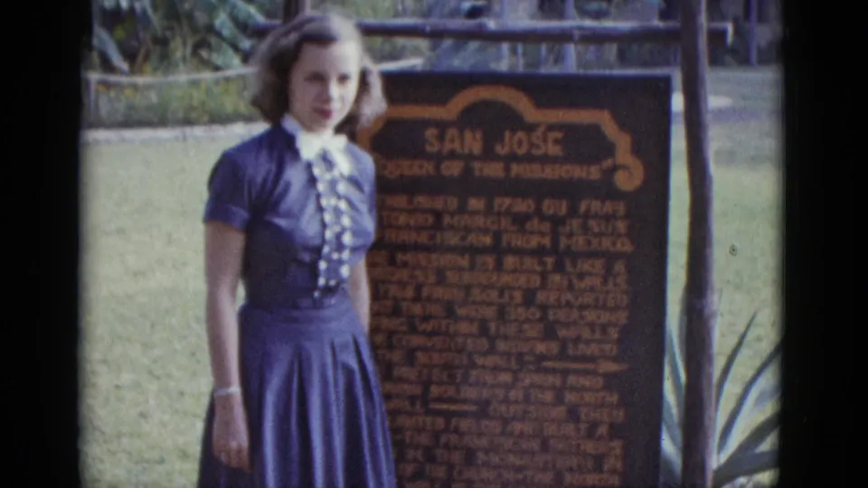 8mm colour frame of a young woman in early-1950s dress beside the San José Mission marker; visible text names Fray Antonio Margil de Jesús and a founding date of 1720.