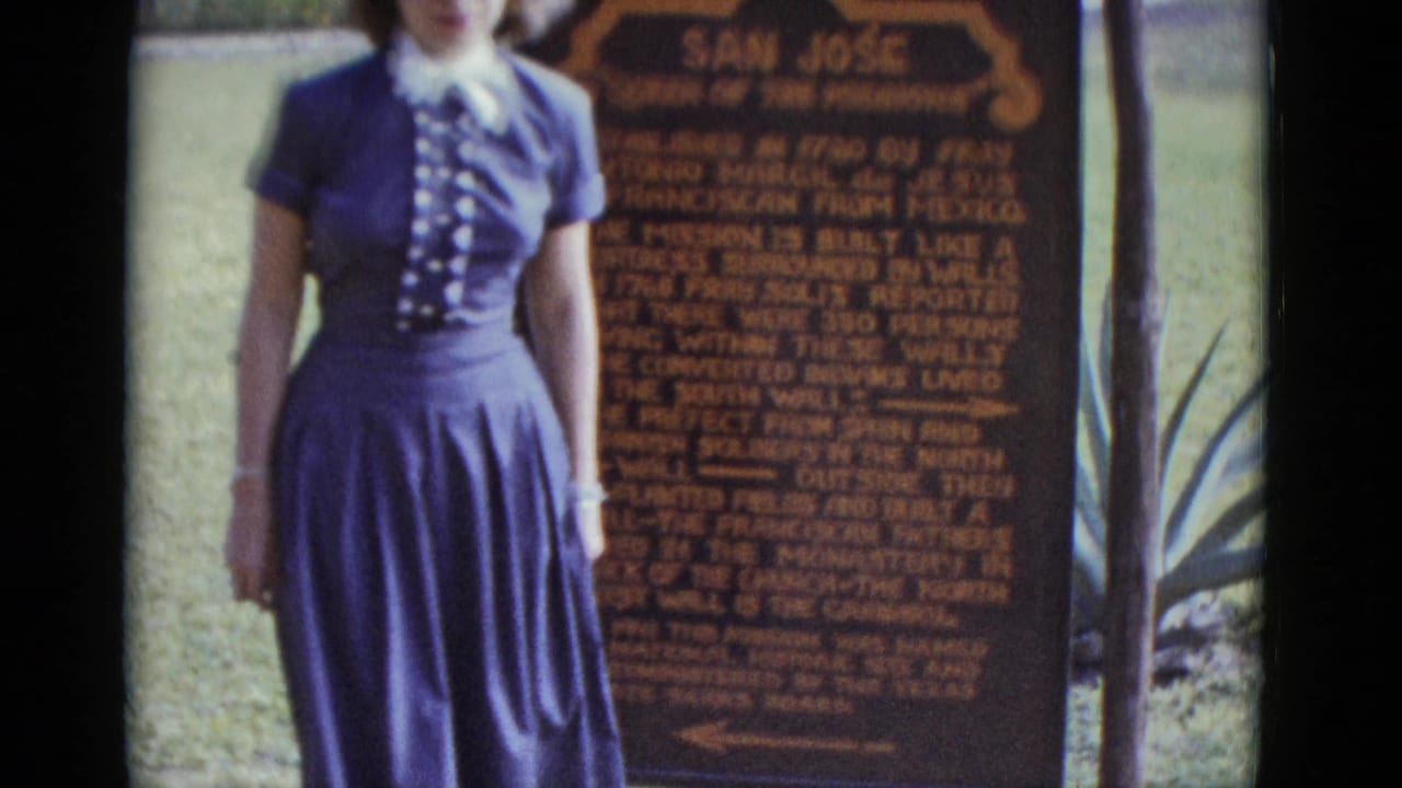 Closer view of the same woman in a blue dress beside the Mission San José historical marker, sign text more legible.