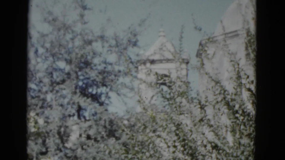Final pan frame from a 1952 8mm travel film showing a white steepled structure and possible rounded architectural feature above a tree line, attributed to New Orleans.